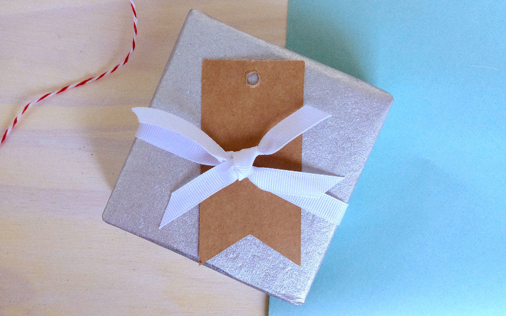A minimally wrapped Christmas gift with a white ribbon and kraft tag